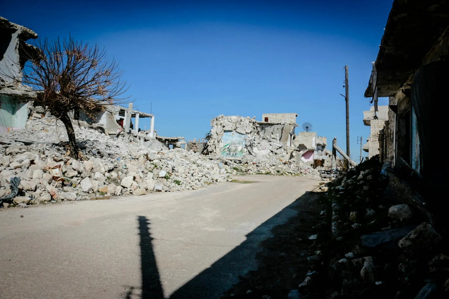 A desolate street in Idlib, Syria, showing the aftermath of conflict with destroyed buildings and rubble.