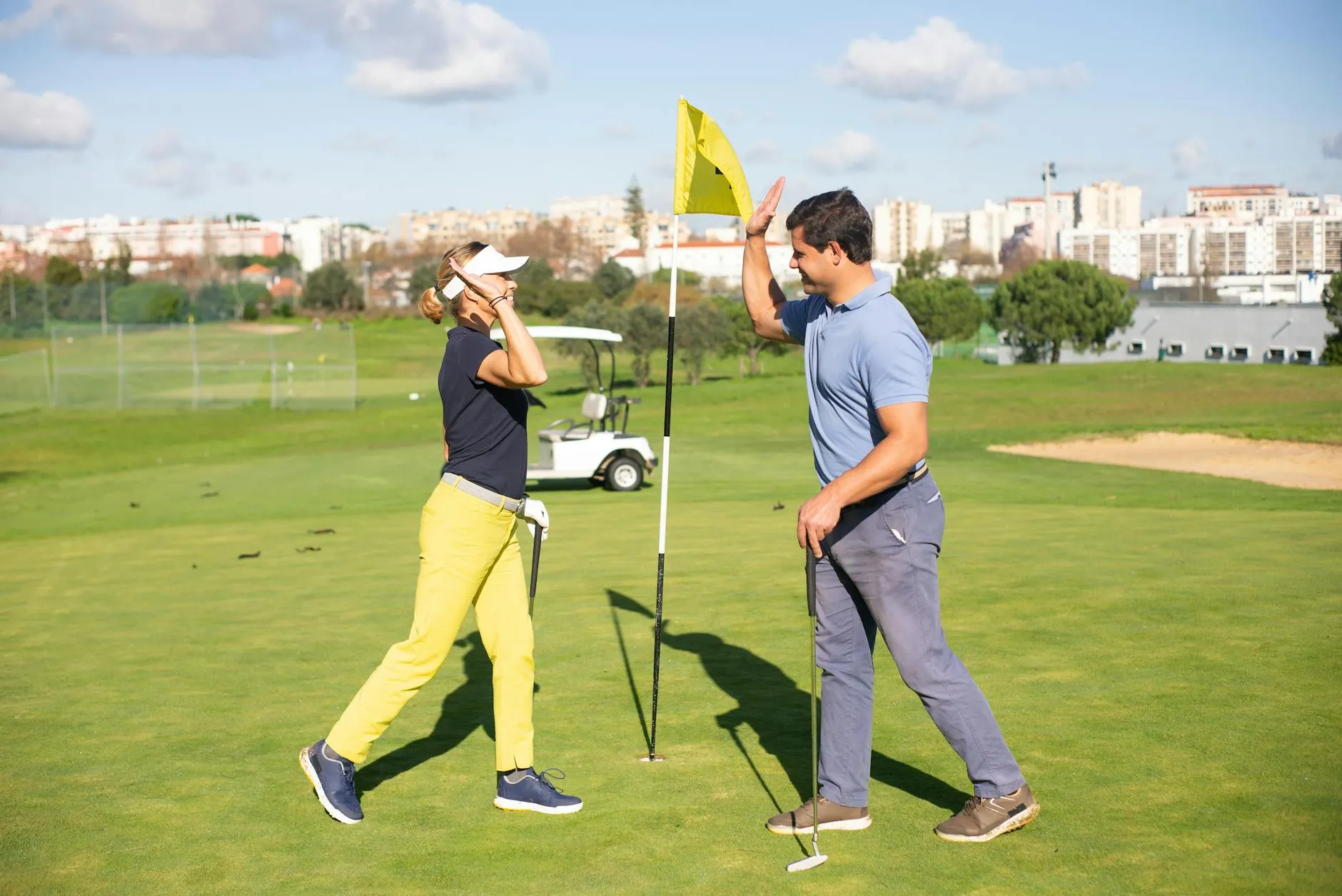 Two golfers celebrate a successful shot with a high five on a sunny green course.