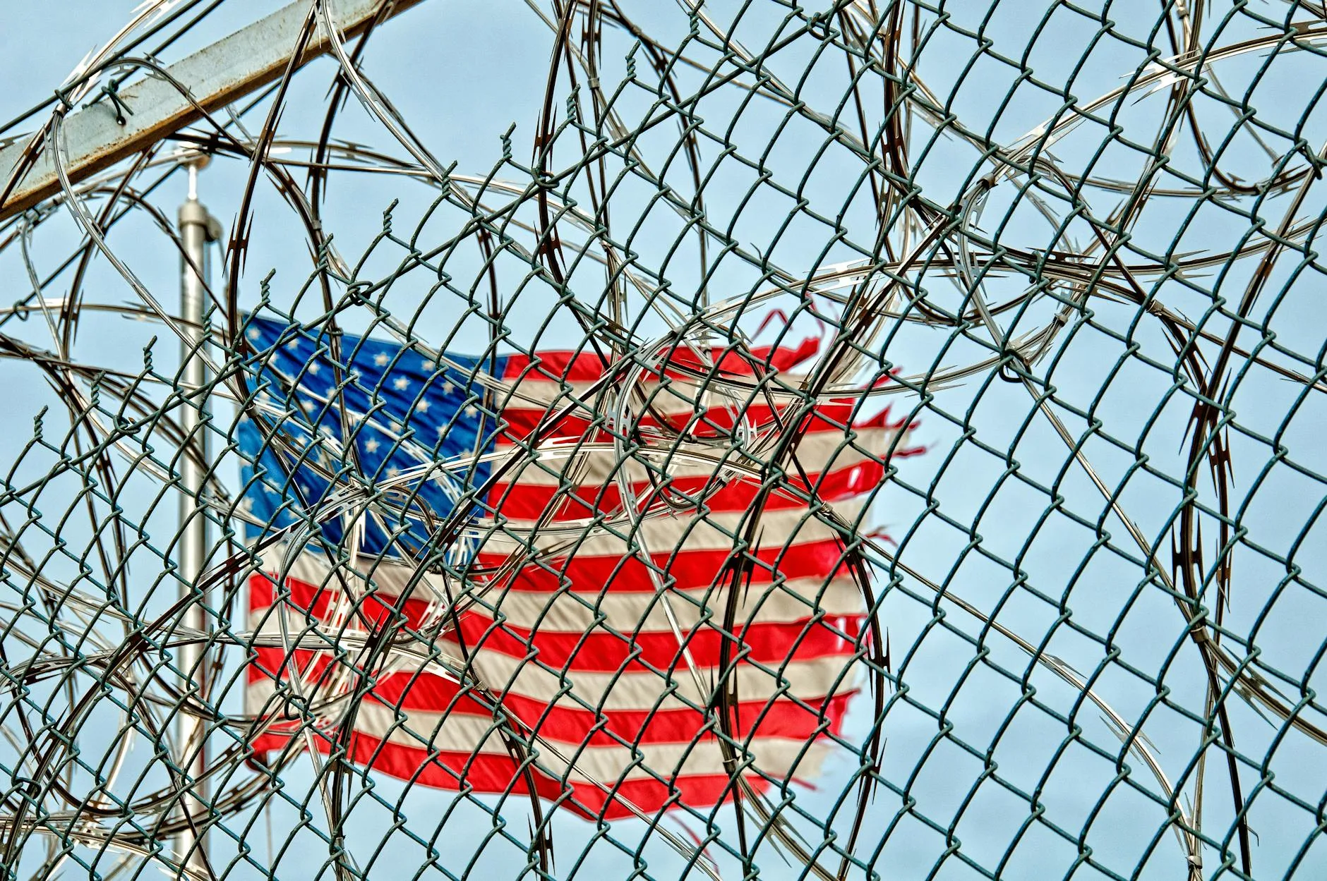 A symbolic image of the USA flag seen through barbed wire, representing freedom and protection.