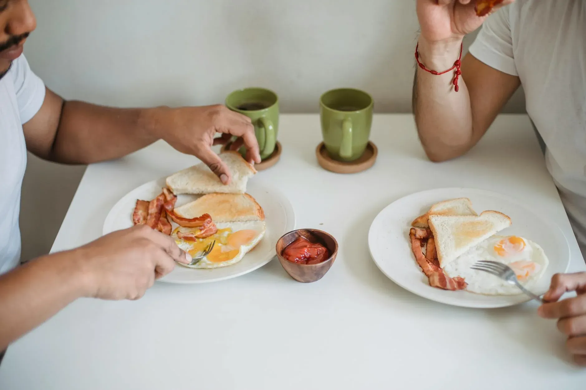 Two friends savoring a simple yet satisfying breakfast of bacon, eggs, and toast in a warm, sunlit kitchen.