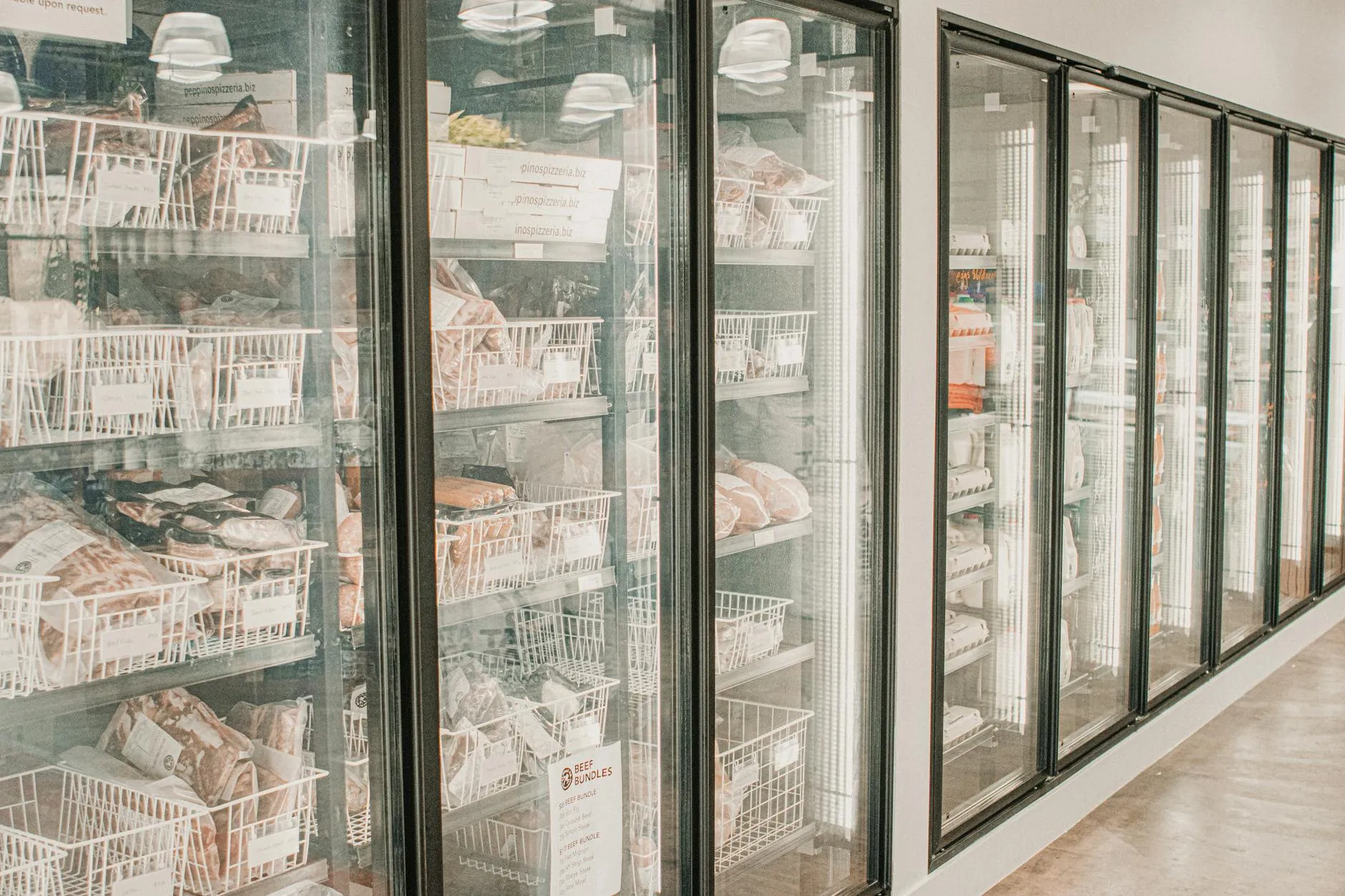 A clear view of frozen meat products arranged neatly in a retail freezer with transparent doors, highlighting freshness and organization.