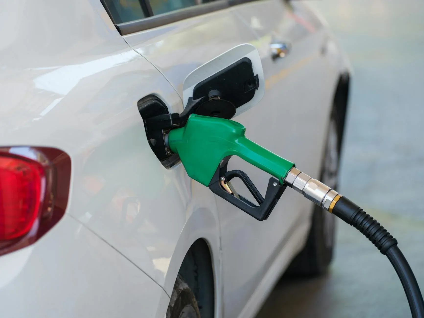 A detailed close-up of a green fuel nozzle inserting into a white car's gas tank at a modern gas station.