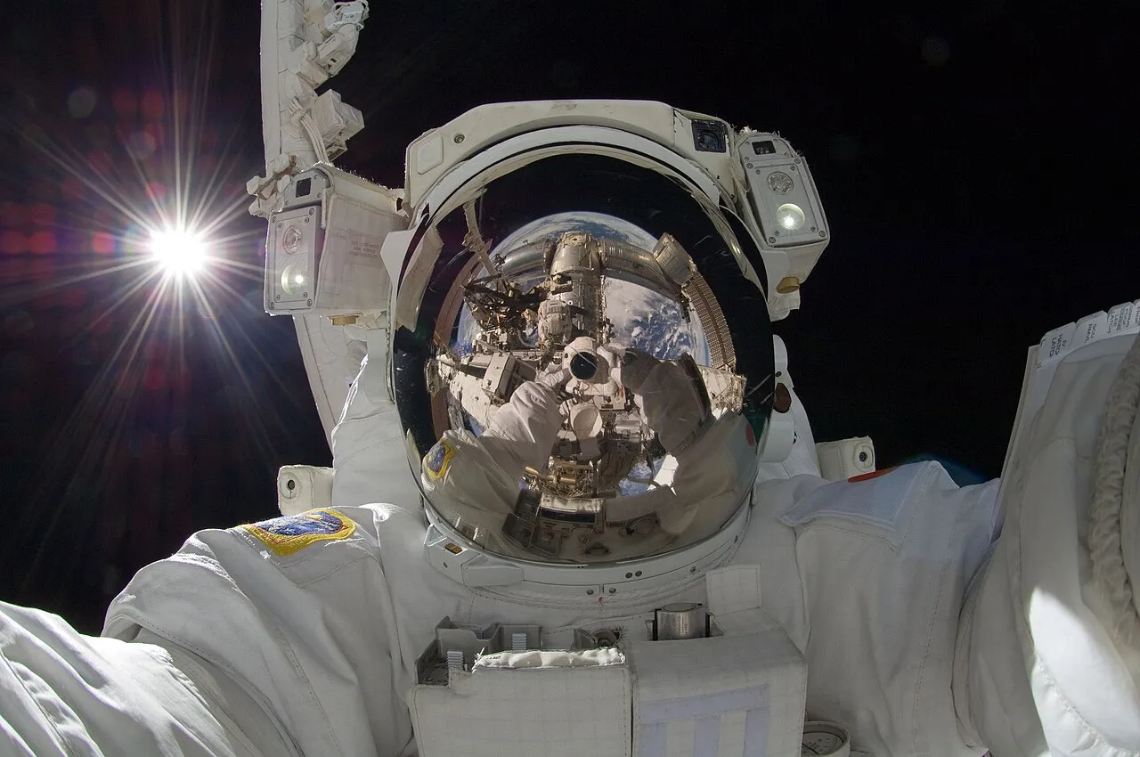 Akihiko Hoshide captures a photo of his helmet visor during a spacewalk on the International Space Station, showcasing the Earth and the station's robotic arm.