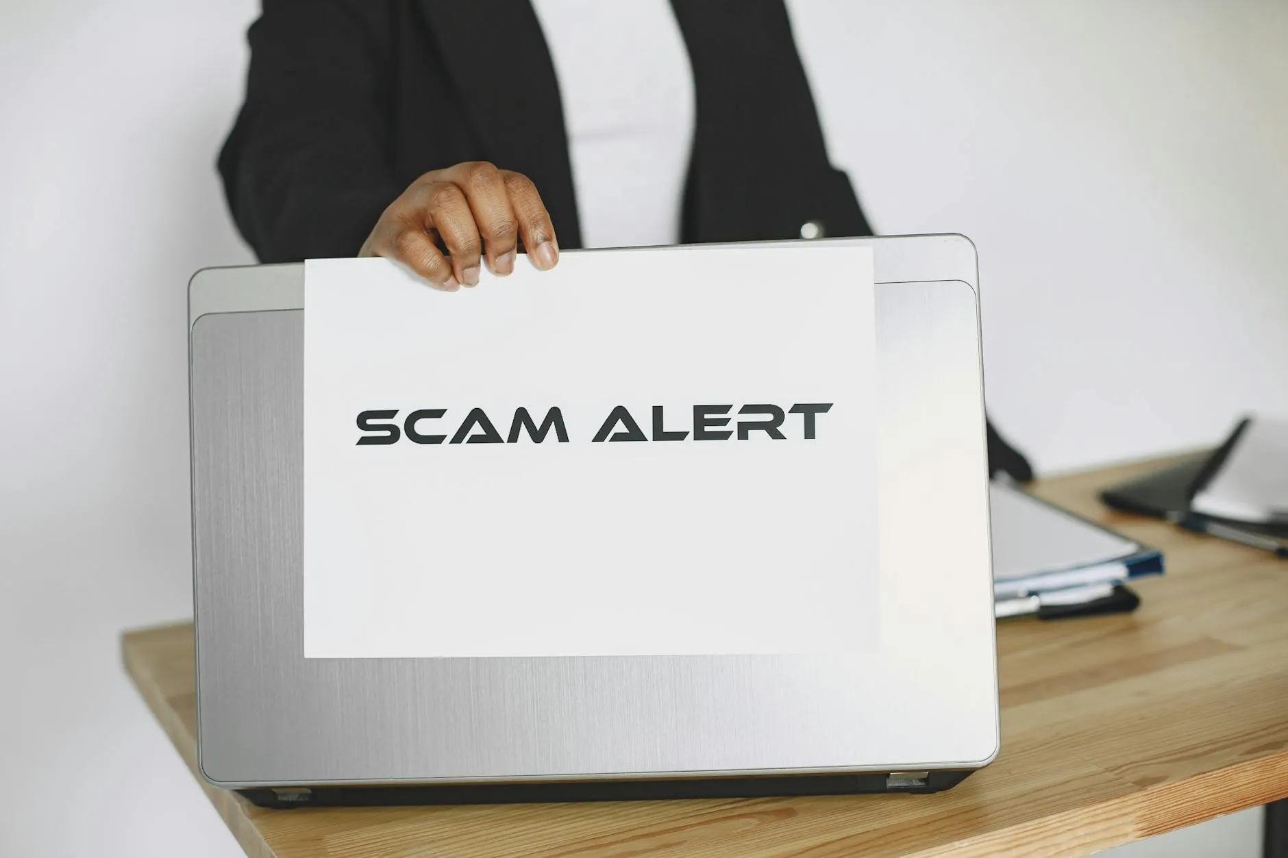 En person holder et skilt med en scam-advarsel over en laptop, der illustrerer online svindel og phishing. Billedet er velegnet til artikler om cybersikkerhed og digitale trusler.