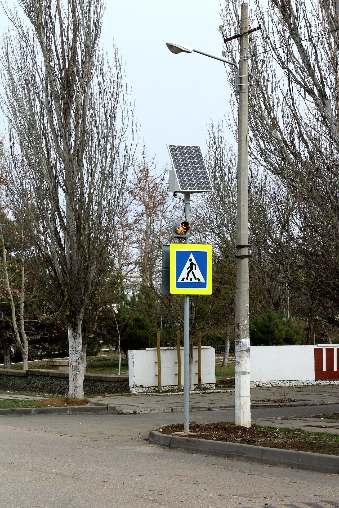 Et blinkende gult trafiklys ved et fodgængerfelt. Lyset er drevet af en solcelle og er placeret nær en skole.