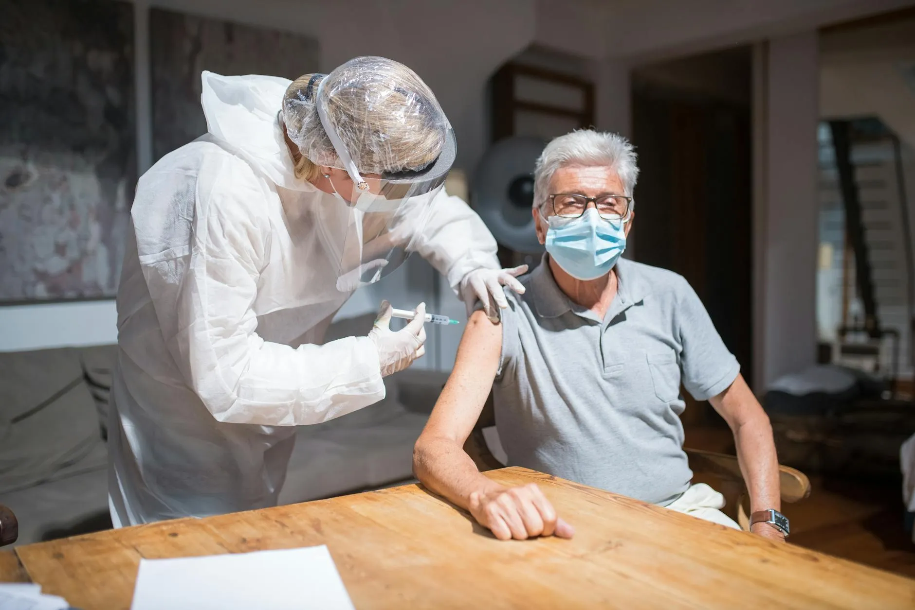 En sundhedsmedarbejder giver en COVID-19-vaccine til en ældre mand i et indendørs miljø. Billedet symboliserer tryghed, sundhed og forebyggelse.