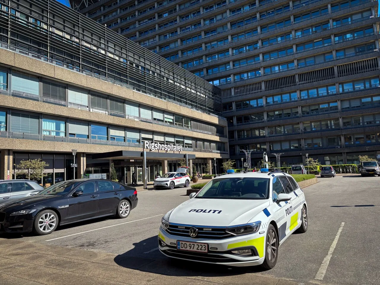 En dansk politibil holder parkeret foran hovedindgangen til Rigshospitalet i København. Billedet viser politiets tilstedeværelse ved et større hospital.