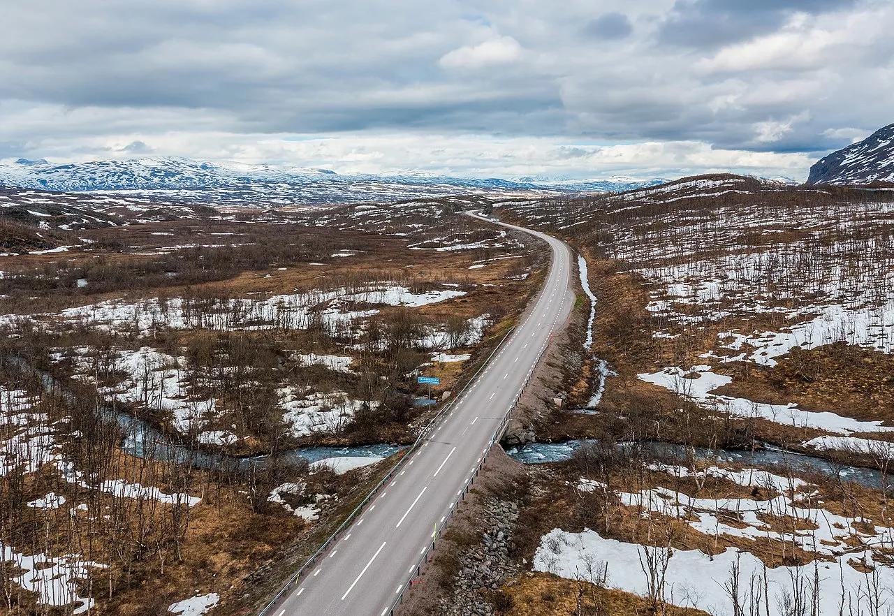 E 10-vej i området nær Låktatjåkka i Kiruna, Norrbottens län, Sverige, fotograferet i juni 2022. Gearggejohka-floden løber nedenfor vejen og understreger det barske nordlige landskab.