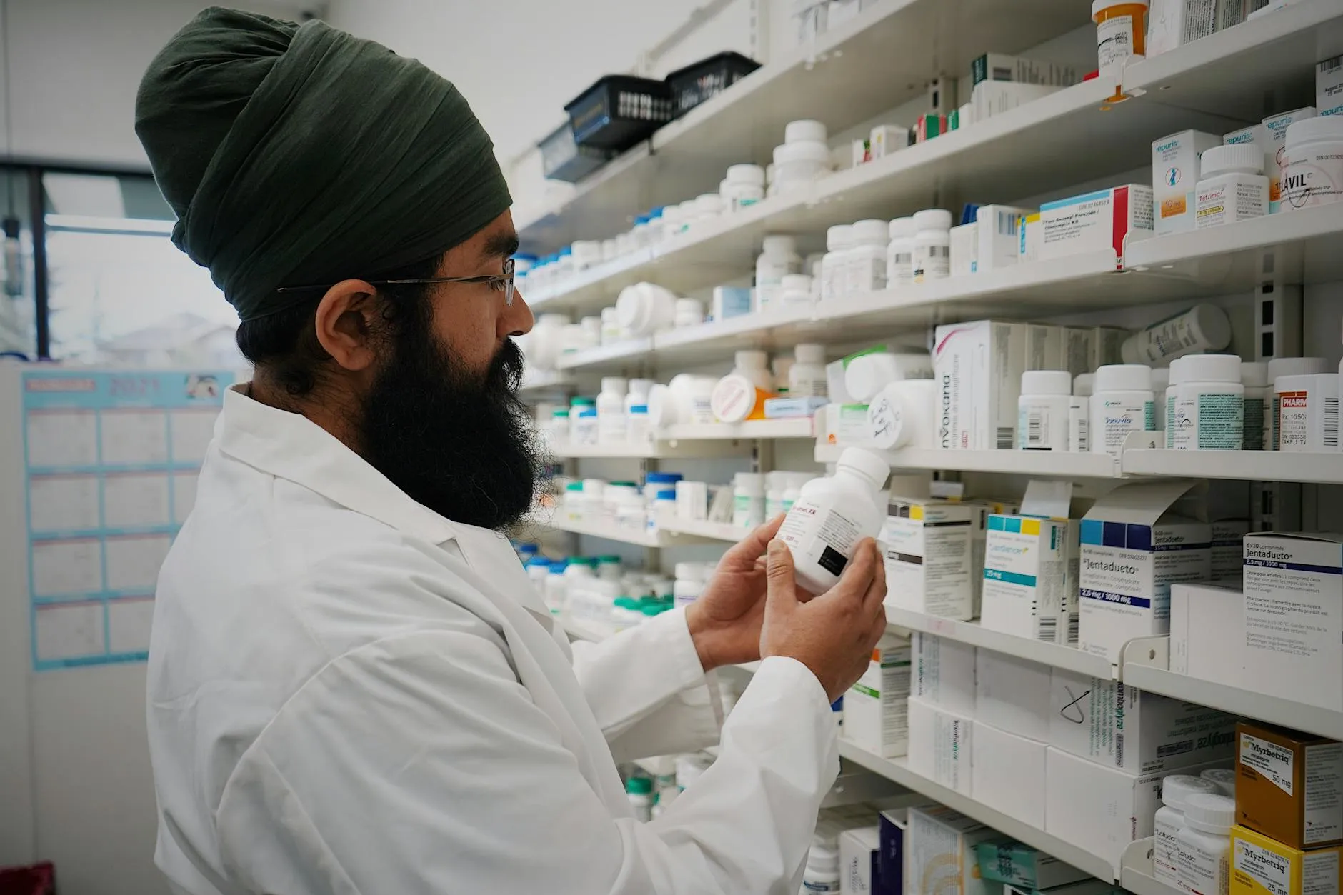 En farmaceut med turban organiserer hylder i et apotek. Billedet formidler fokus på sundhed og rådgivning.
