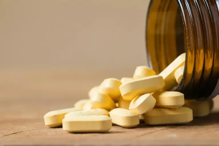 En glaskapselbeholder med ravfarvede kapsler, der vælter ud på en hvid baggrund. Motivet understreger medicin/kosttilskud og et rent, klinisk udtryk.