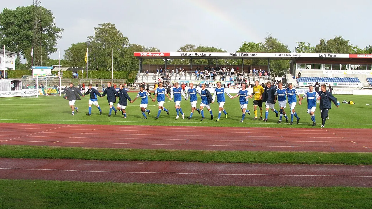 Fodboldkamp mellem Lyngby BK og FC Fyn på Lyngby Stadion, som endte 2-1. Stemningen og spillet fanges midt i kampen.