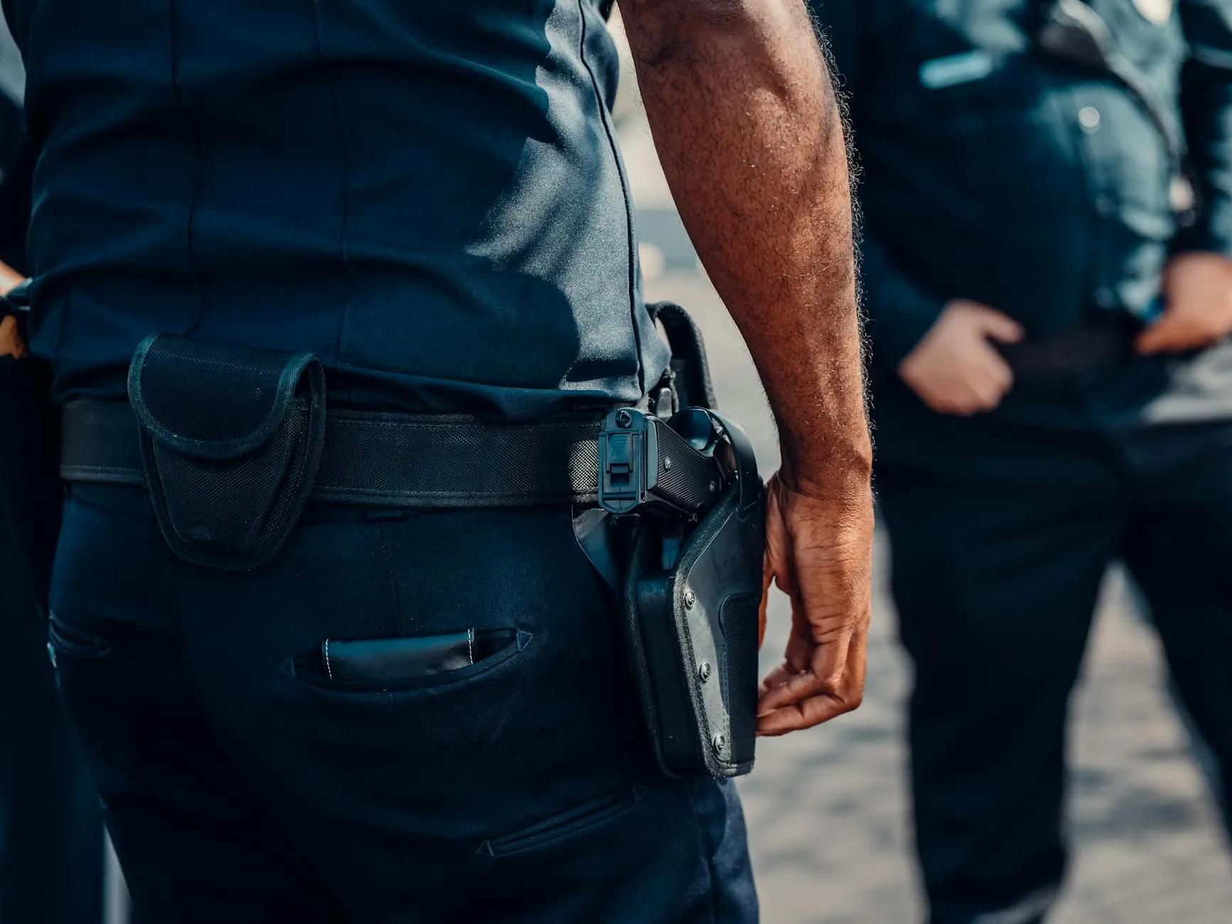 Close-up af en politibetjents pistol, der sidder sikkert i hylsteret ved hoften. Billedet signalerer professionalisme og beredskab.