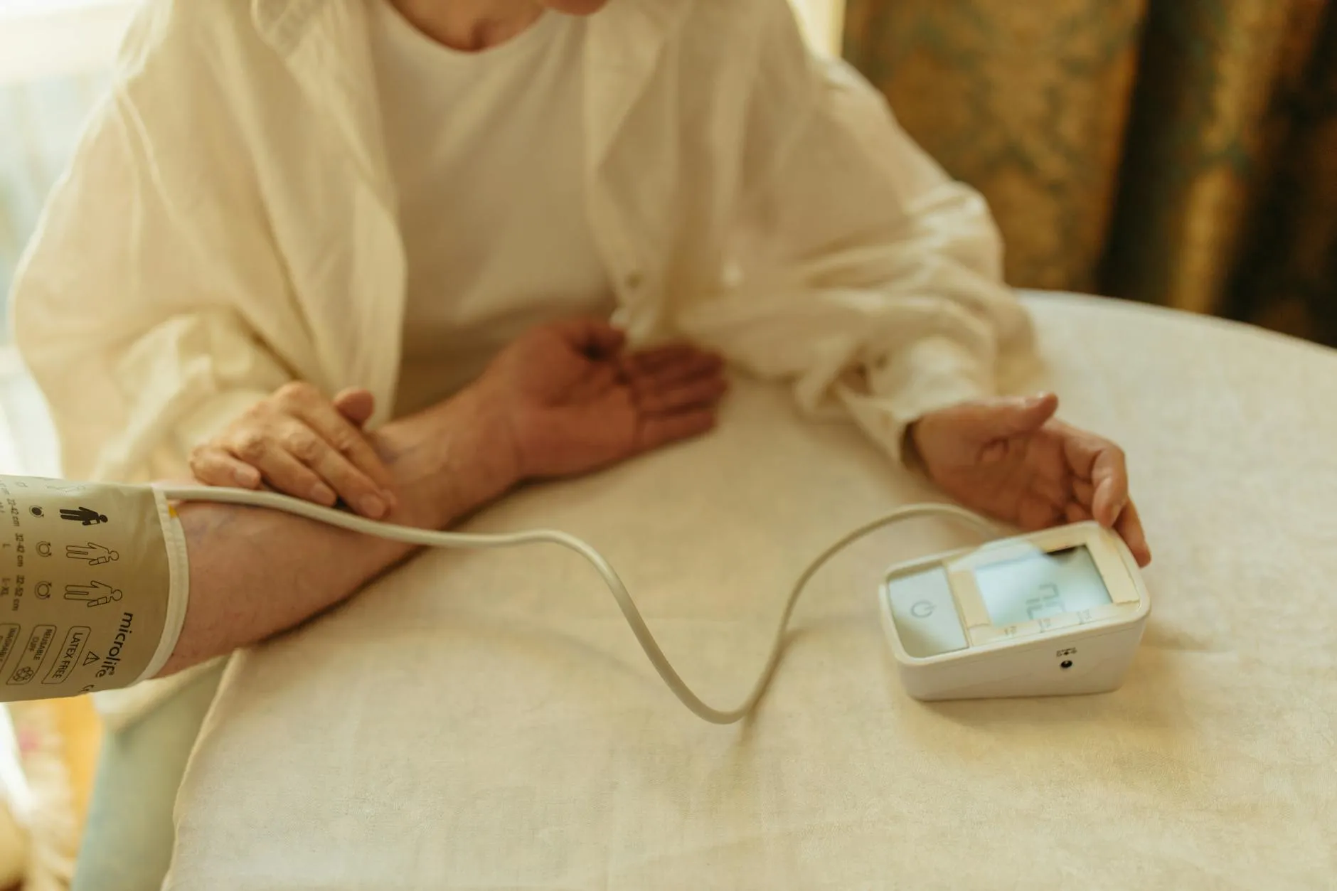 En senior tjekker sit blodtryk med en digital blodtryksmåler i hjemmet. Situationen illustrerer selvmonitorering og sundhedsovervågning.