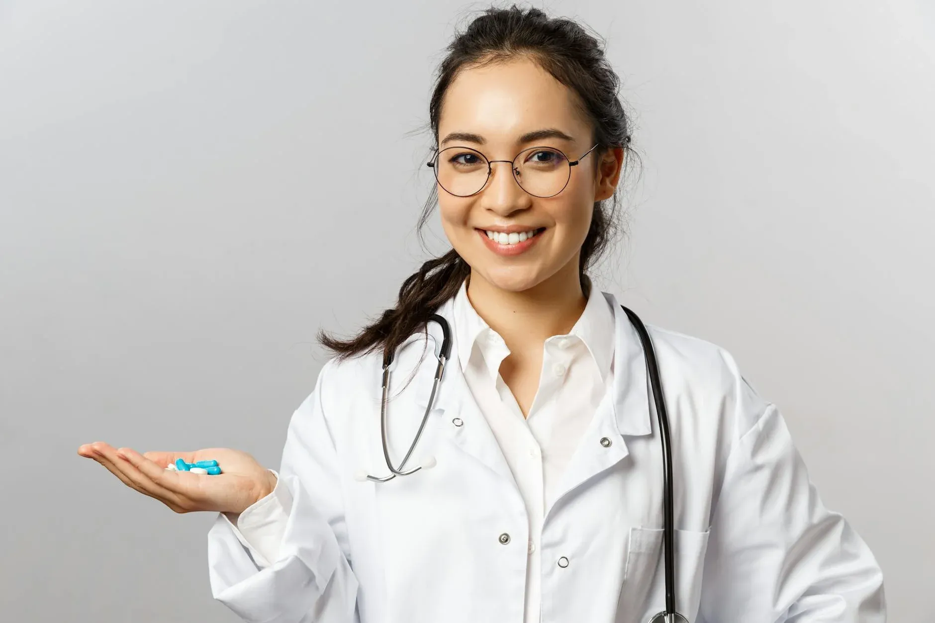 En kvindelig læge smiler og holder piller, mens hun formidler tryghed og behandling. Billedet understøtter temaer som sundhed, medicin og patientomsorg.
