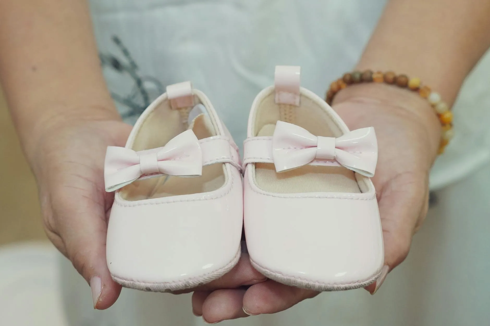 Et par små babysko med sløjfer holdes i hænderne, perfekt til en baby-girl annoncering eller gaveidé. Stemningen er varm og kærlig.