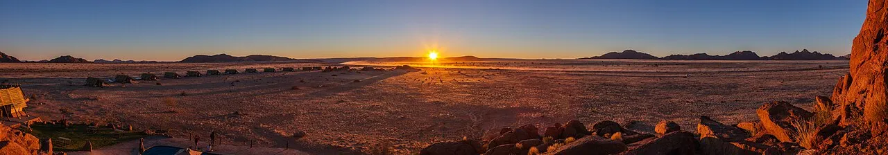 En dramatisk solnedgang over sandlandskabet i Namib-ørkenen. Farverne i himlen spejler sig i det barske ørkenmiljø.