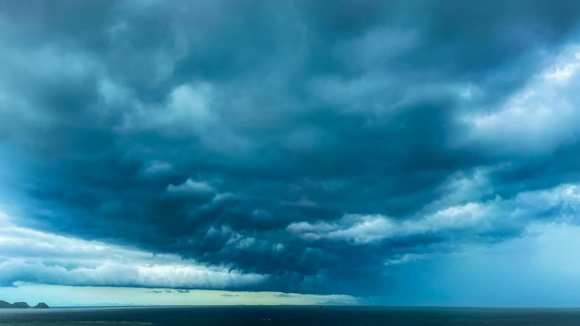 Mørke stormskyer hænger lavt over et vidtstrakt hav. Stemningen er dramatisk og uvejret er tydeligt på vej.