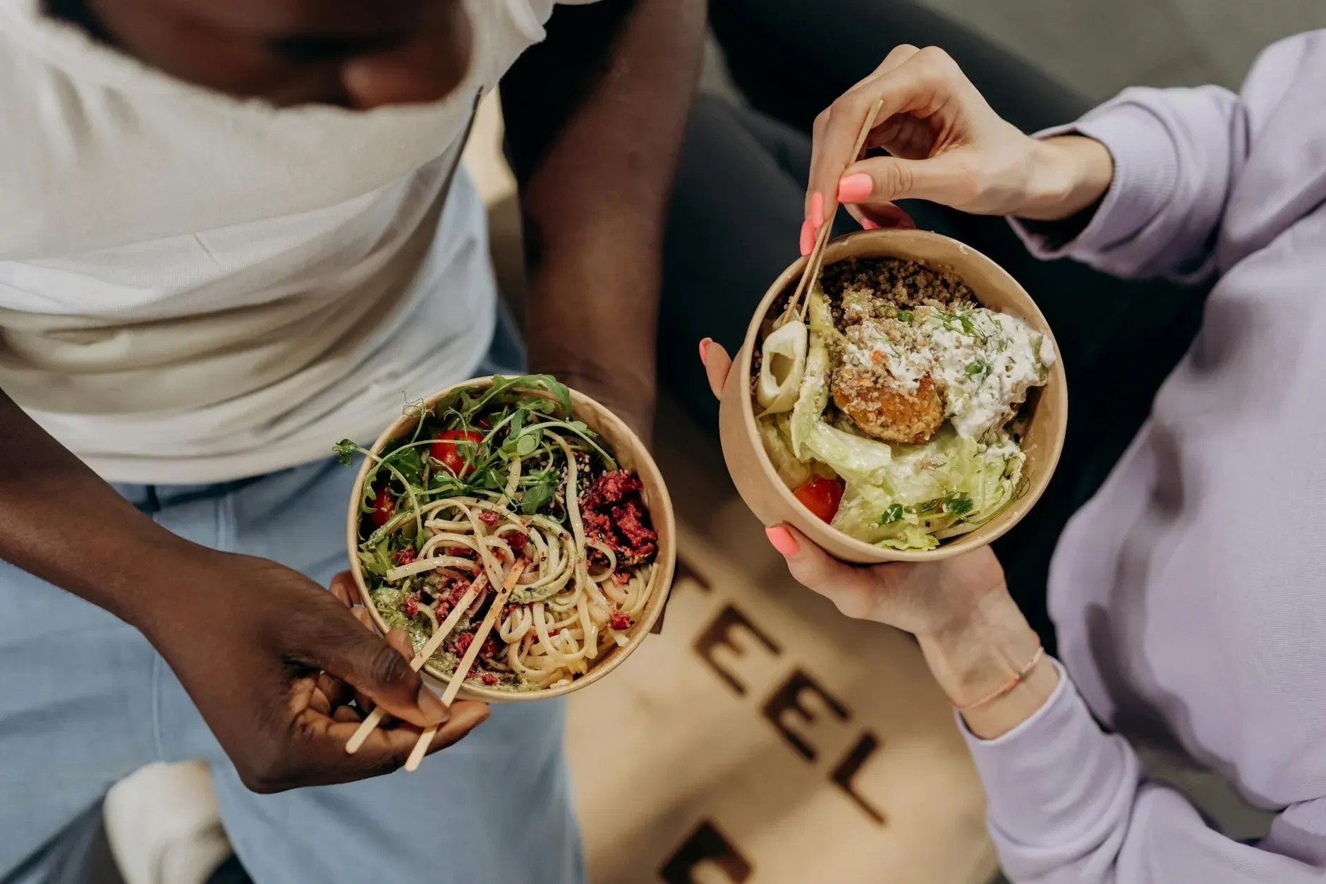 To personer holder skåle med salat og pasta, der understreger et sundt og bevidst madvalg. Stemningen signalerer balance mellem smag og sundhed.