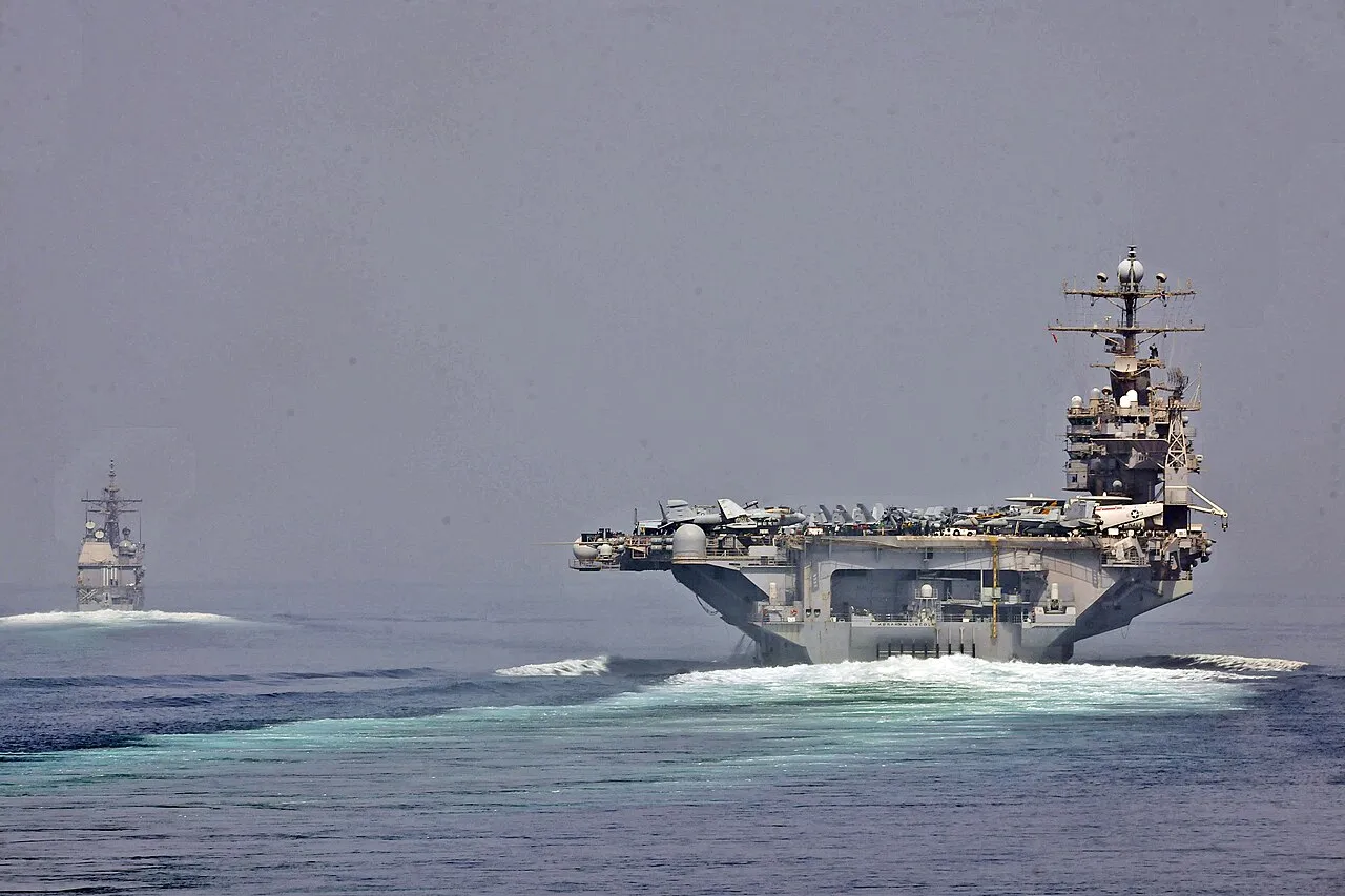 USS Cape St. George og hangarskibet USS Abraham Lincoln sejler gennem strædet ved Hormuz under maritime sikkerhedsoperationer. Billedet illustrerer skibenes passage i et af verdens mest strategiske farvande.