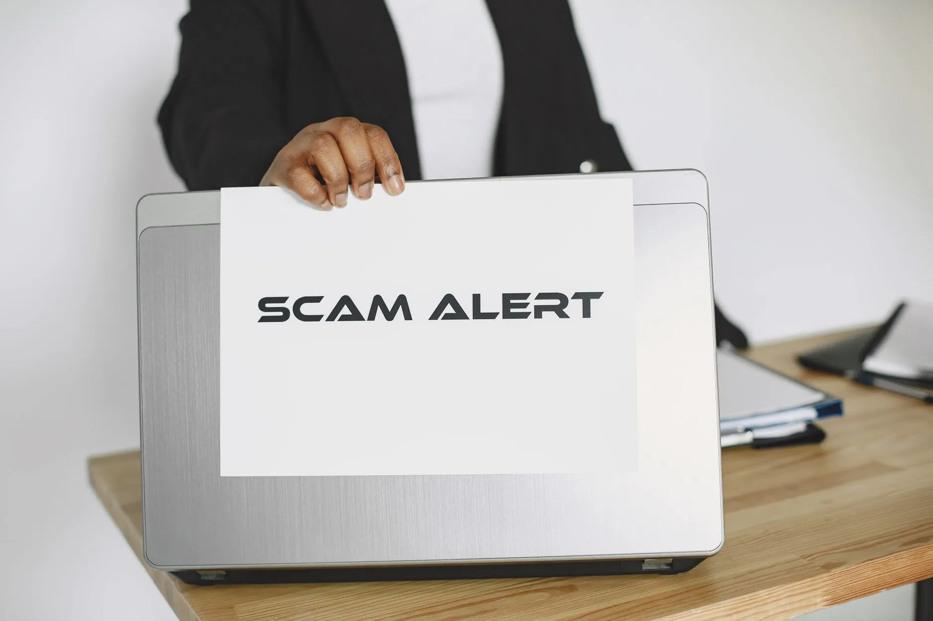 En person holder et skilt med “scam alert” foran en laptop, mens der advares mod online svindel. Billedet signalerer digital sikkerhed og opmærksomhed på phishing.