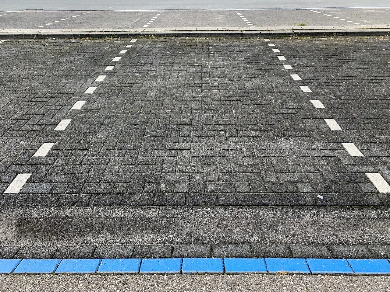 Parkeringspladser i en blå parkeringszone markeret med blå brostensindlæg. Billedet viser tydelige afmærkninger på belægningen.