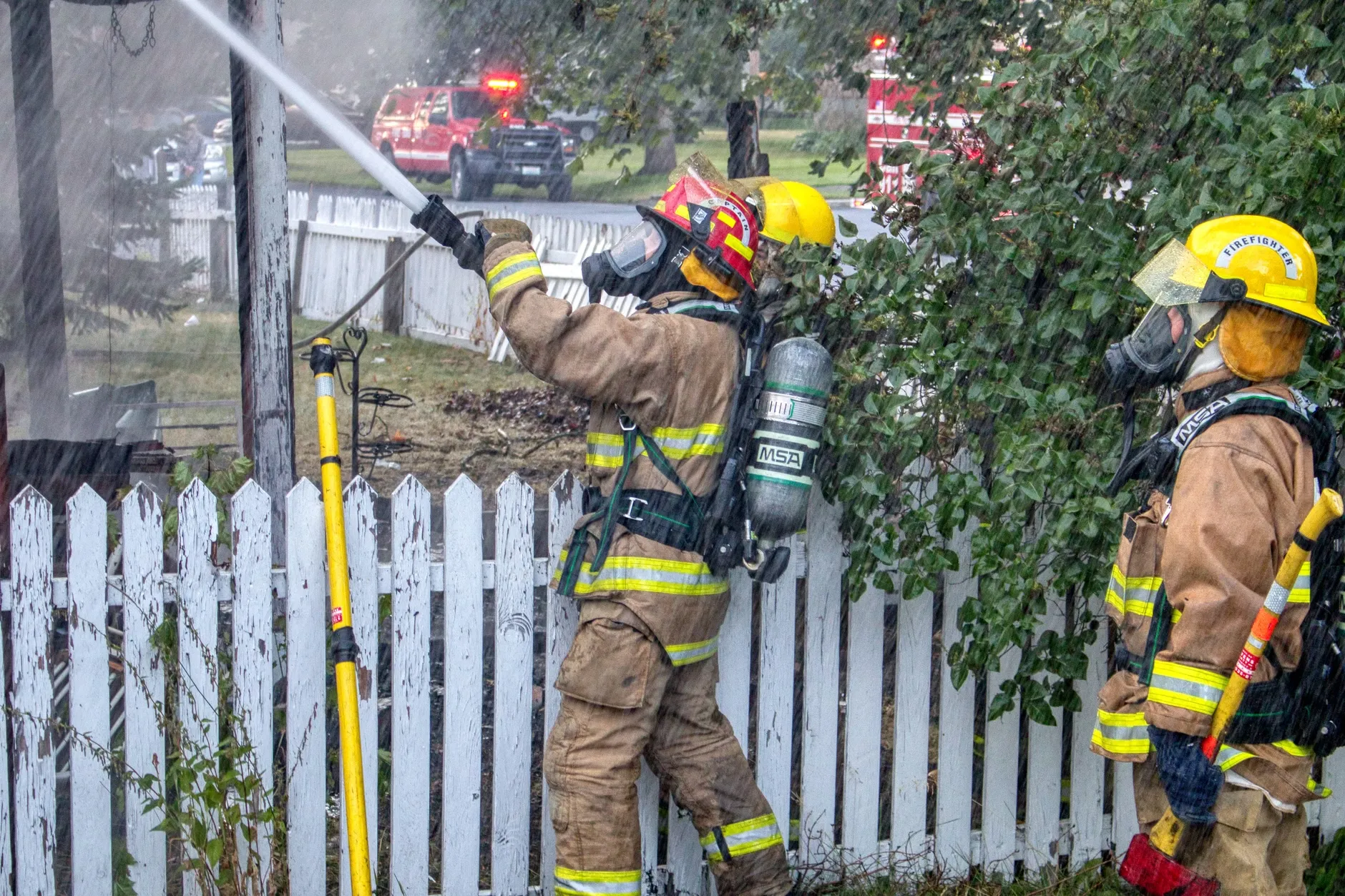 Brandmænd i beskyttelsesudstyr slukker en brand i Chewelah, WA. Scenen illustrerer samarbejde og indsats under en aktiv brandsituation.
