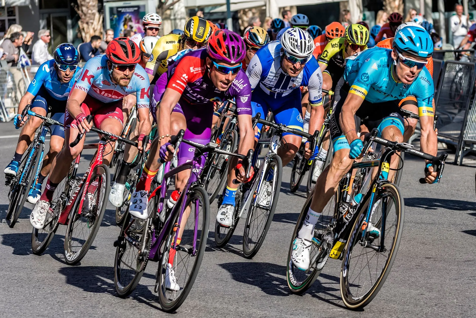En gruppe konkurrerende cyklister kører gennem byens gader i Alicante. Billedet fanger fart, energi og bystemning under løbet.