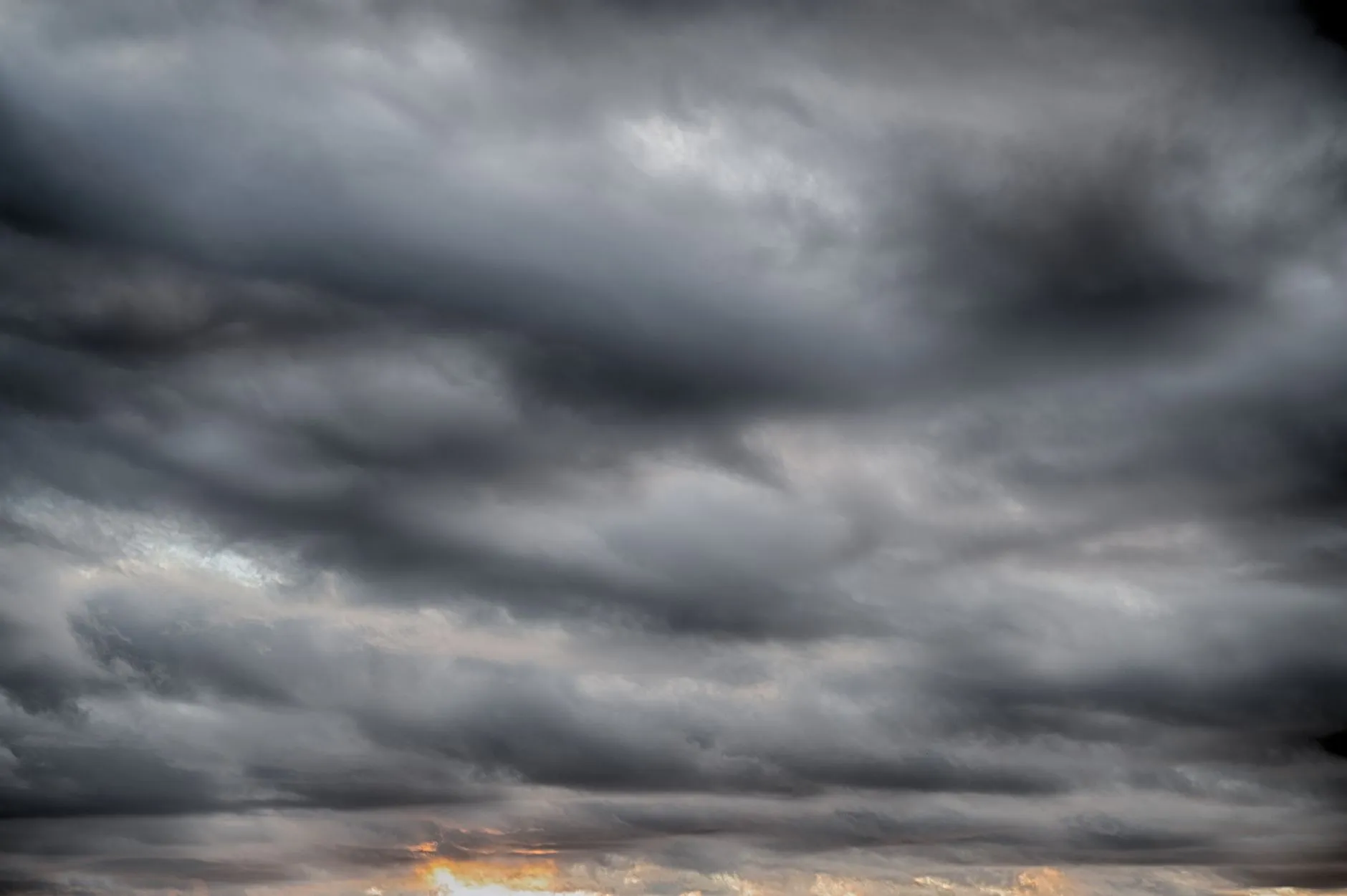 Mørke stormskyer samler sig over landskabet under en dramatisk solnedgang. Stemningen antyder, at en tordenbyge kan være på vej.