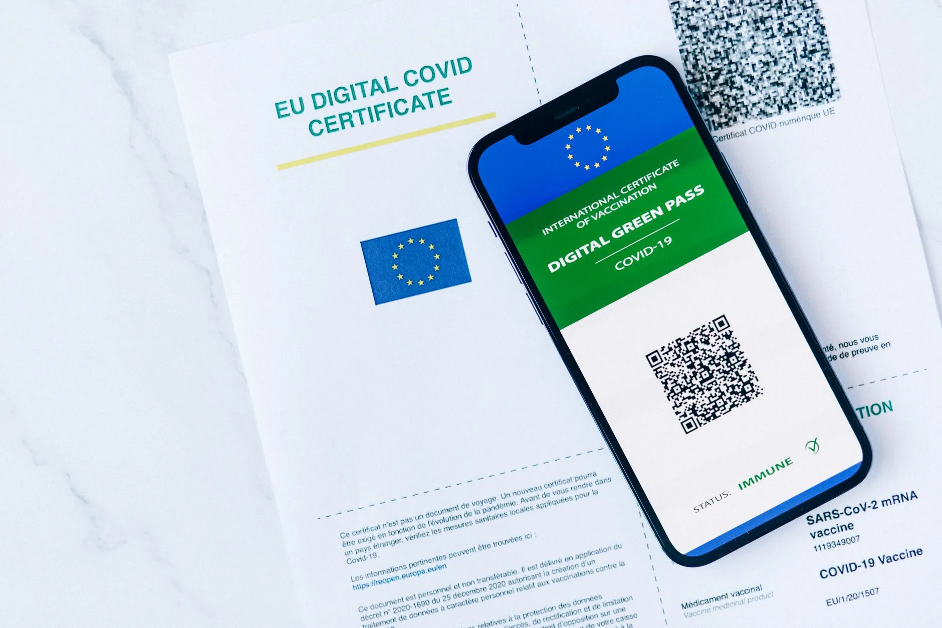 EU Digital COVID Certificate vises på en smartphone sammen med en papirversion. Billedet understøtter temaer om vaccinationsdokumentation og digitale certifikater.