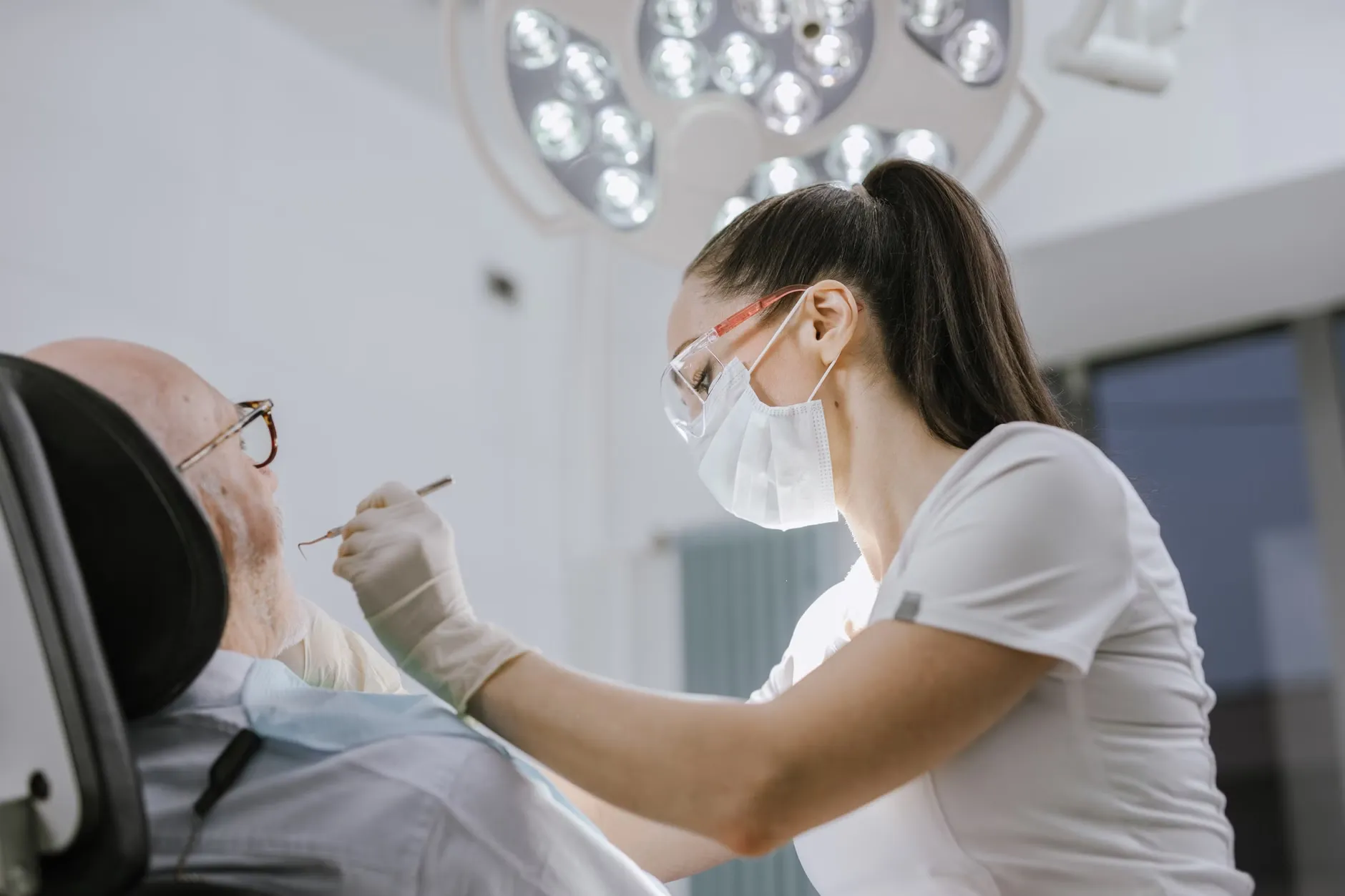 En kvindelig tandlæge arbejder på en patient i et moderne tandlægeklinikmiljø med skarpt, lyst lys.