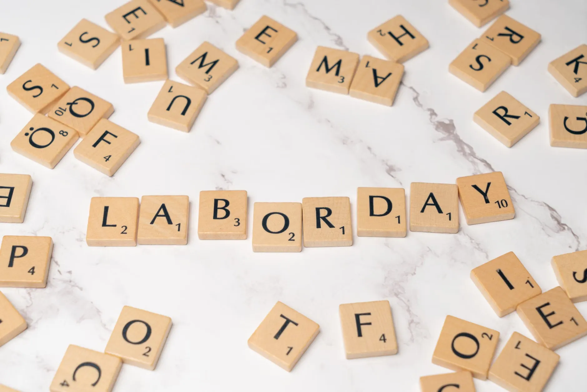 Billedet viser ordet 'Labor Day' dannet af Scrabble-brikker på en marmoryoverflade, symboliserende fejring og kreativitet.