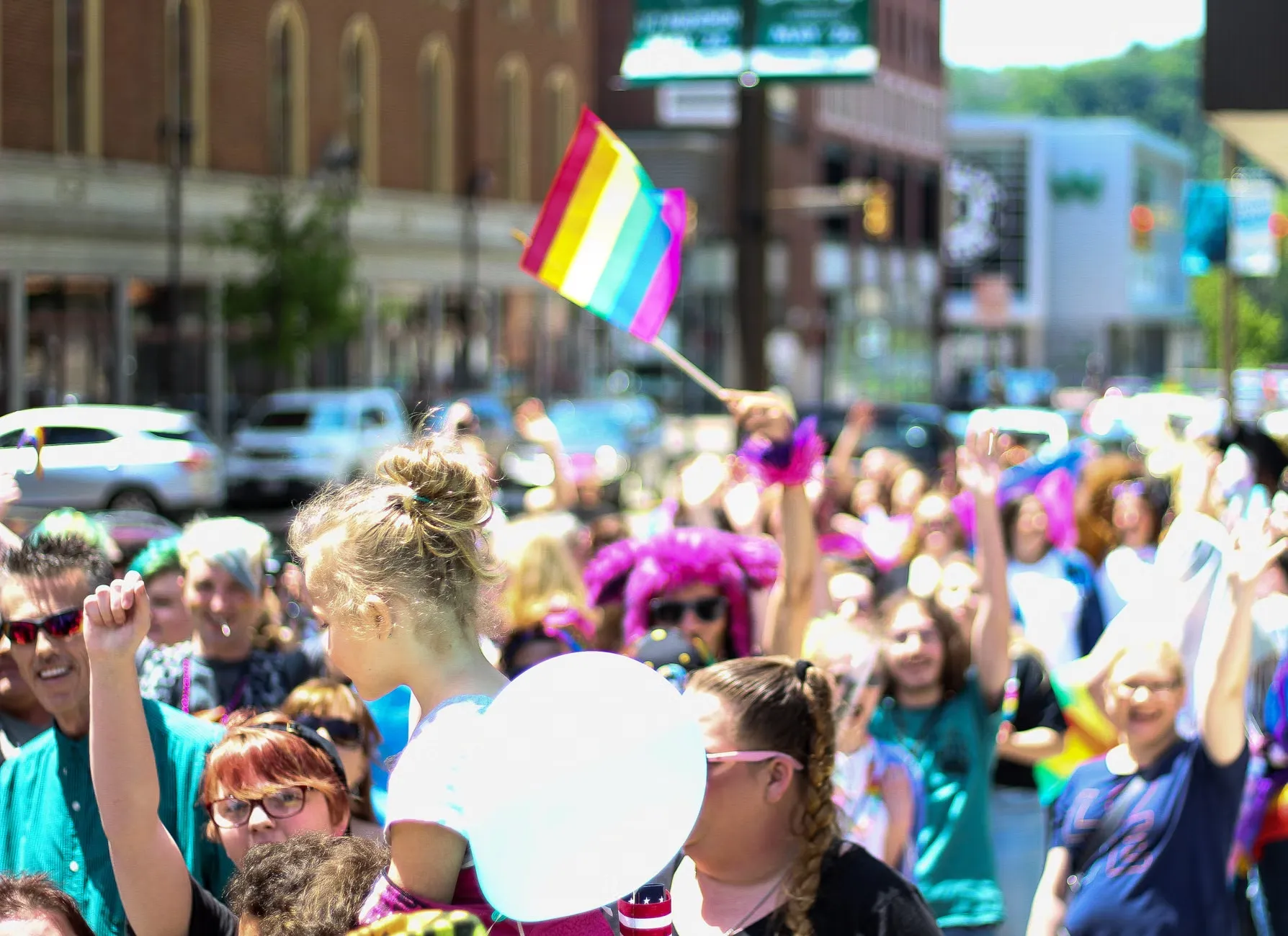 LGBTQ pride parade med multicolored flags og en livlig crowd i en bygade.