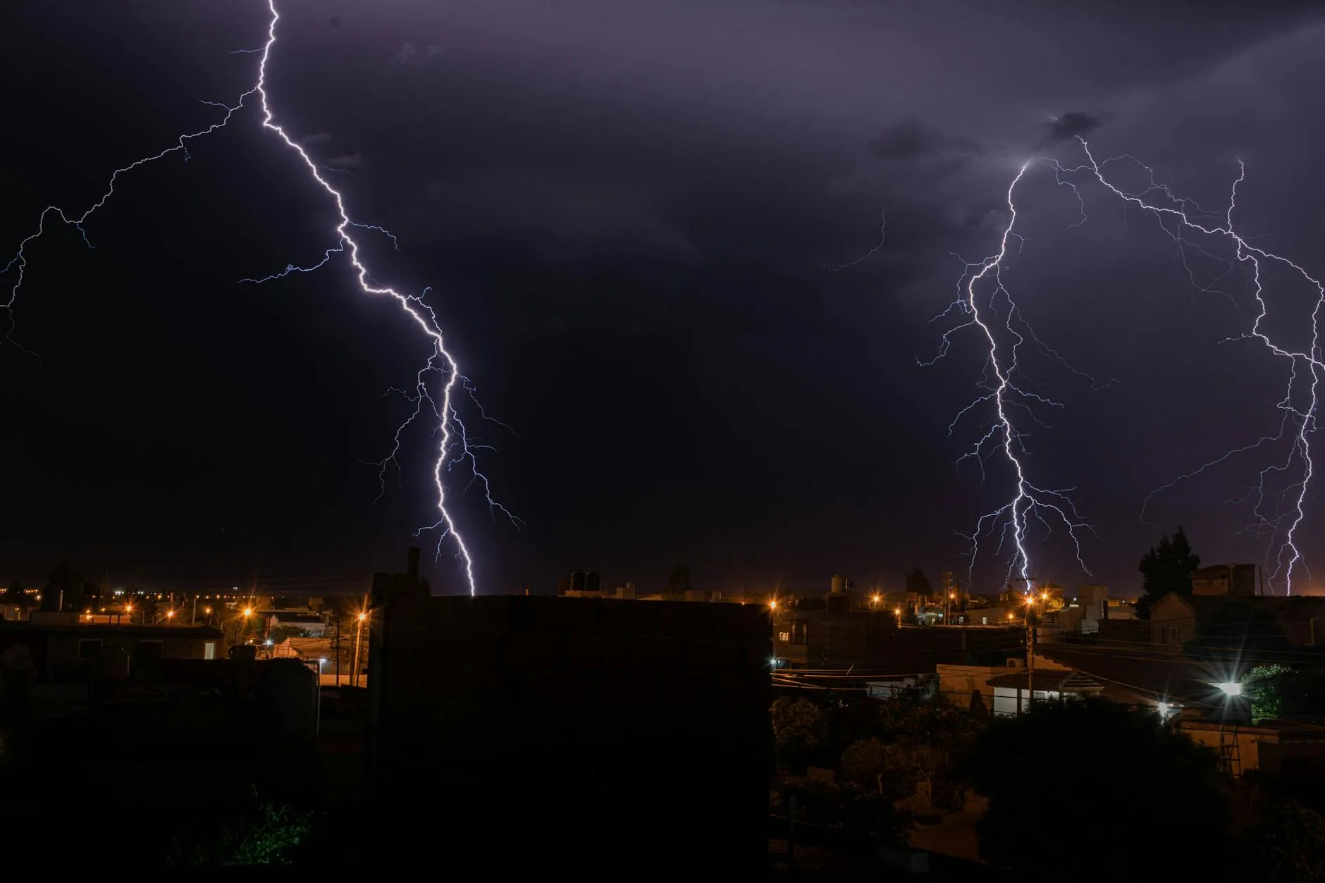 Et kraftigt lynnedslag oplyser en by i mørket under en natlig tordenstorm. Stemningen fremhæver naturens intensitet og dramatik.