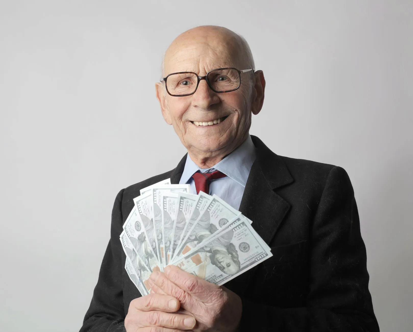 En ældre mand i jakkesæt med briller holder amerikanske dollars. Motivet bruges ofte som symbol på opsparing og økonomisk tryghed.