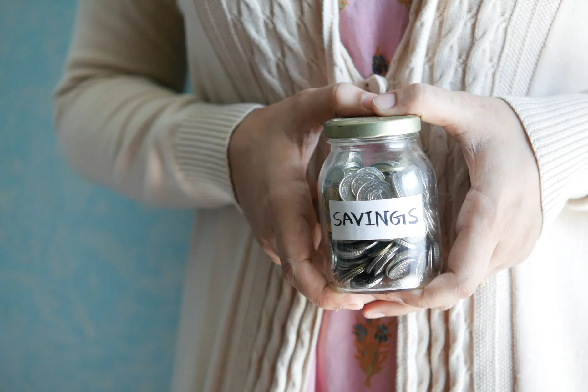 En kvinde holder et glas med teksten "savings", fyldt med mønter. Motivet illustrerer idéen om økonomisk opsparing.