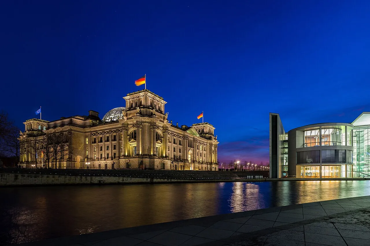 Reichstag-bygningen ses til venstre, mens Paul-Löbe-Haus’ østside ligger til højre langs floden Spree. Billedet er taget i blå time med et roligt, stemningsfuldt lys.