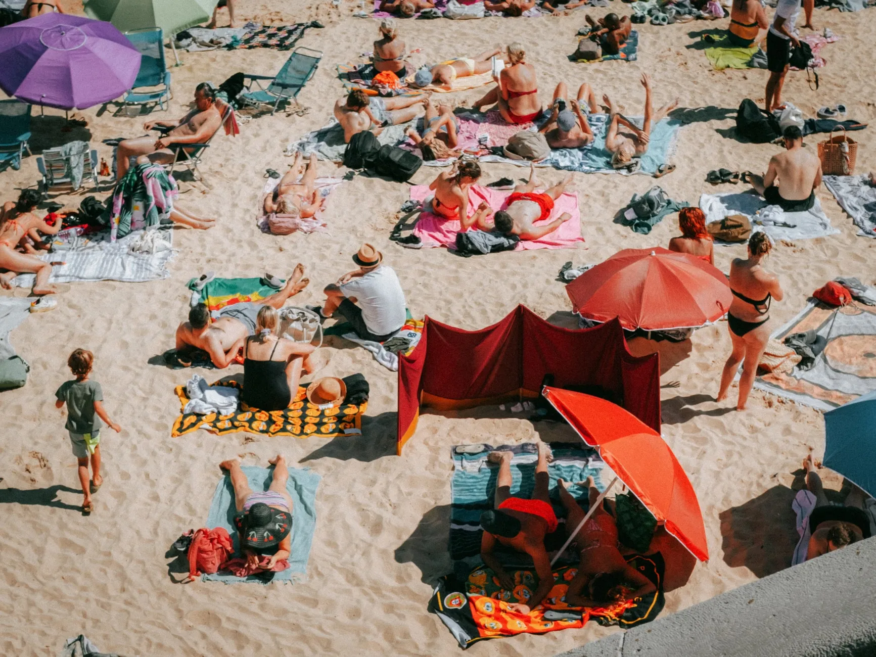En livlig strand i Cascais med mennesker, der solbader og nyder feriestemningen på en solrig dag. Stemningen er afslappet og sommerlig.