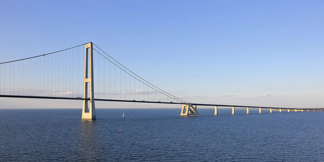Storebæltsbroen ses fra siden med den østlige bro i baggrunden. Et markant ingeniørværk over Storebælt i dagslys.