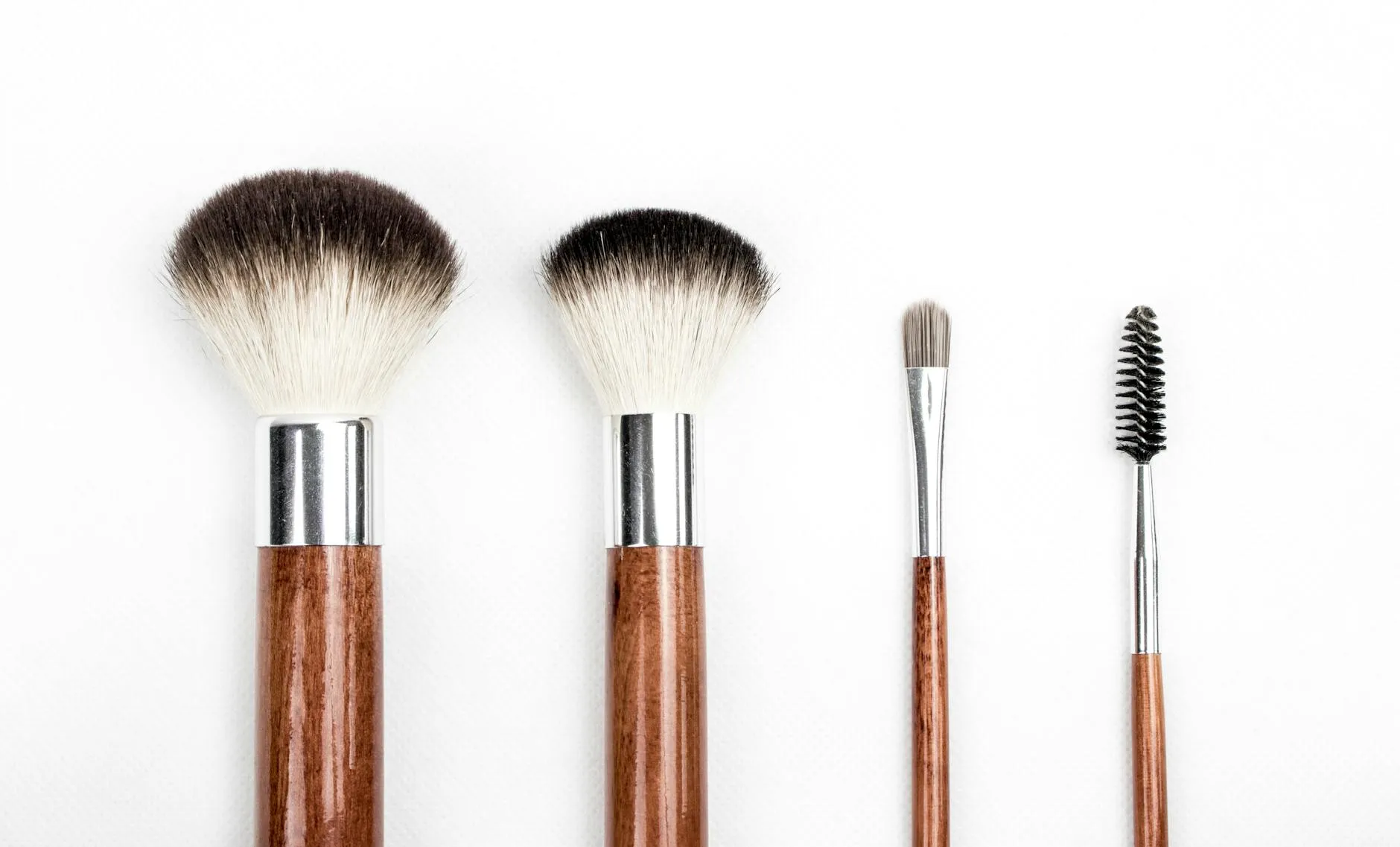 Et stilrent flat lay af fire makeupbørster med skaft i træ mod en ren hvid baggrund. Motivet fremhæver børsternes form og detaljer.