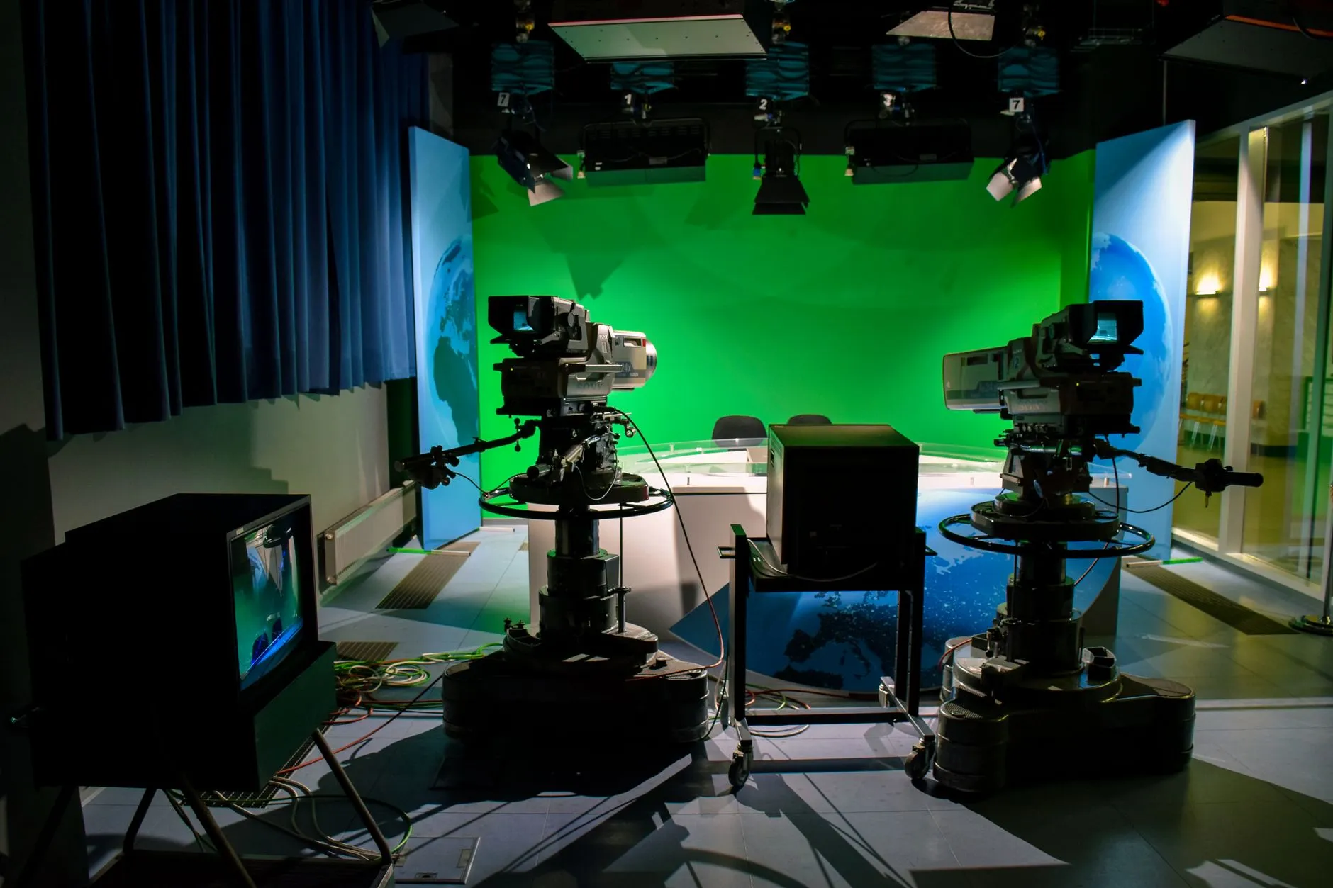 Et TV-studieopsætning med kameraer og en green screen til produktion. Billedet illustrerer moderne video- og medieproduktion i et studiemiljø.