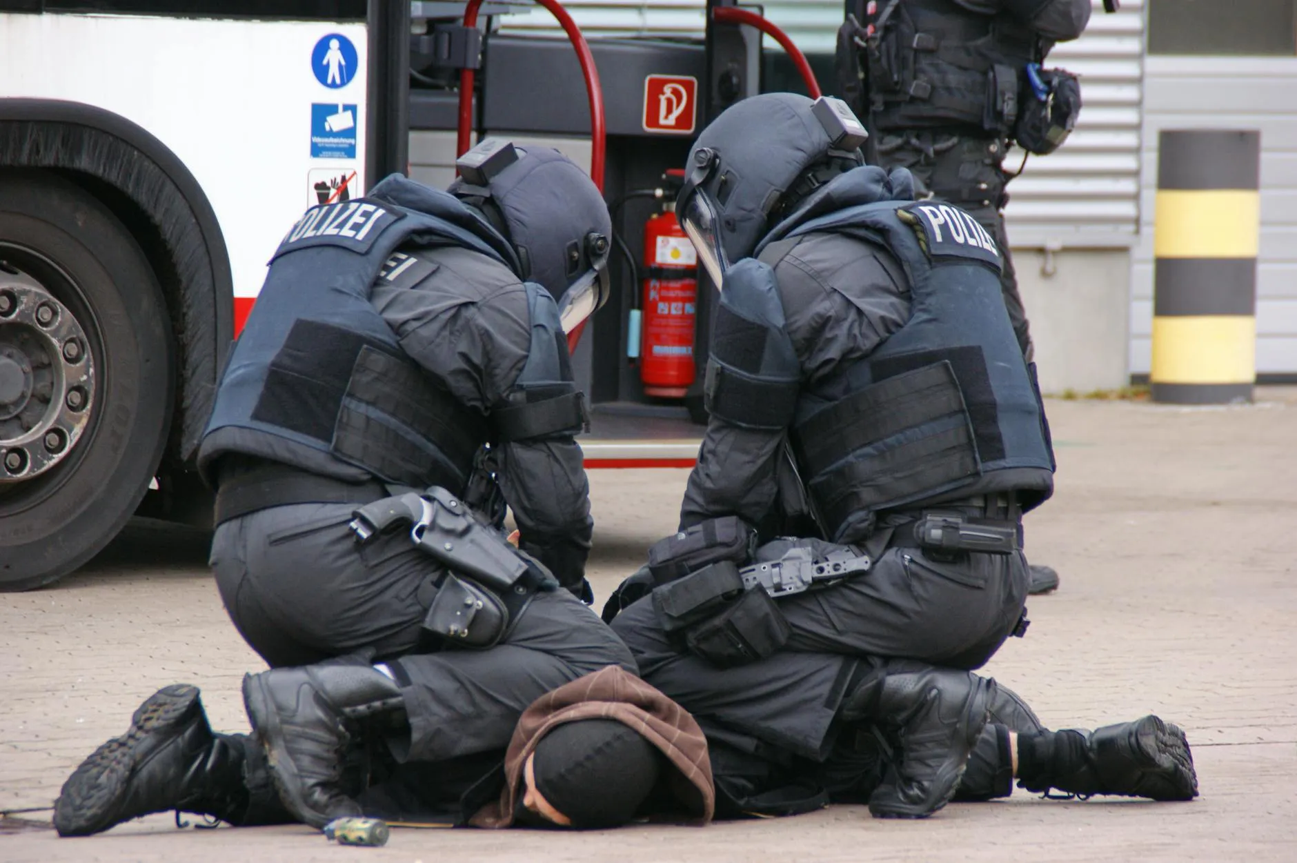 Tysk politi i fuldt udstyr tilbageholder en mistænkt i et byområde i Hamburg. Scenen er fotograferet i en dokumentarisk stil.