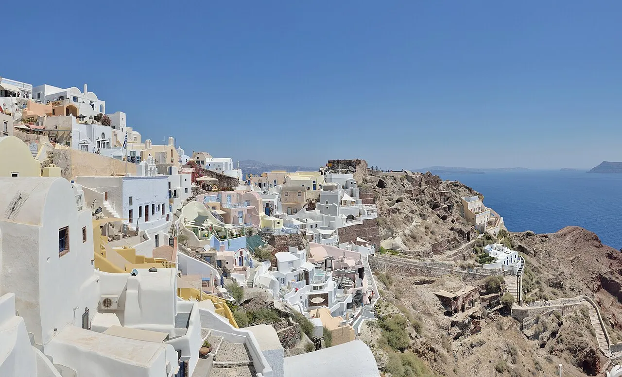 Ia på Santorini med udsigt til ruinerne af en venetiansk borg. Billedet fremhæver kystbyens karakteristiske stemning og historiske spor.