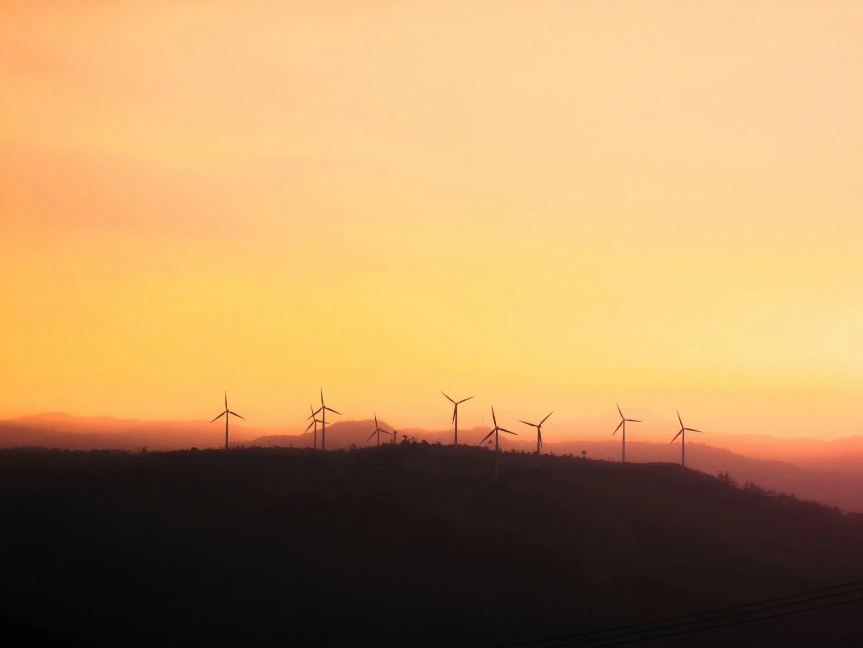 Vindmøller ses som en mørk silhuet mod en solnedgangshimmel. Billedet formidler bæredygtig energiproduktion og grøn omstilling.