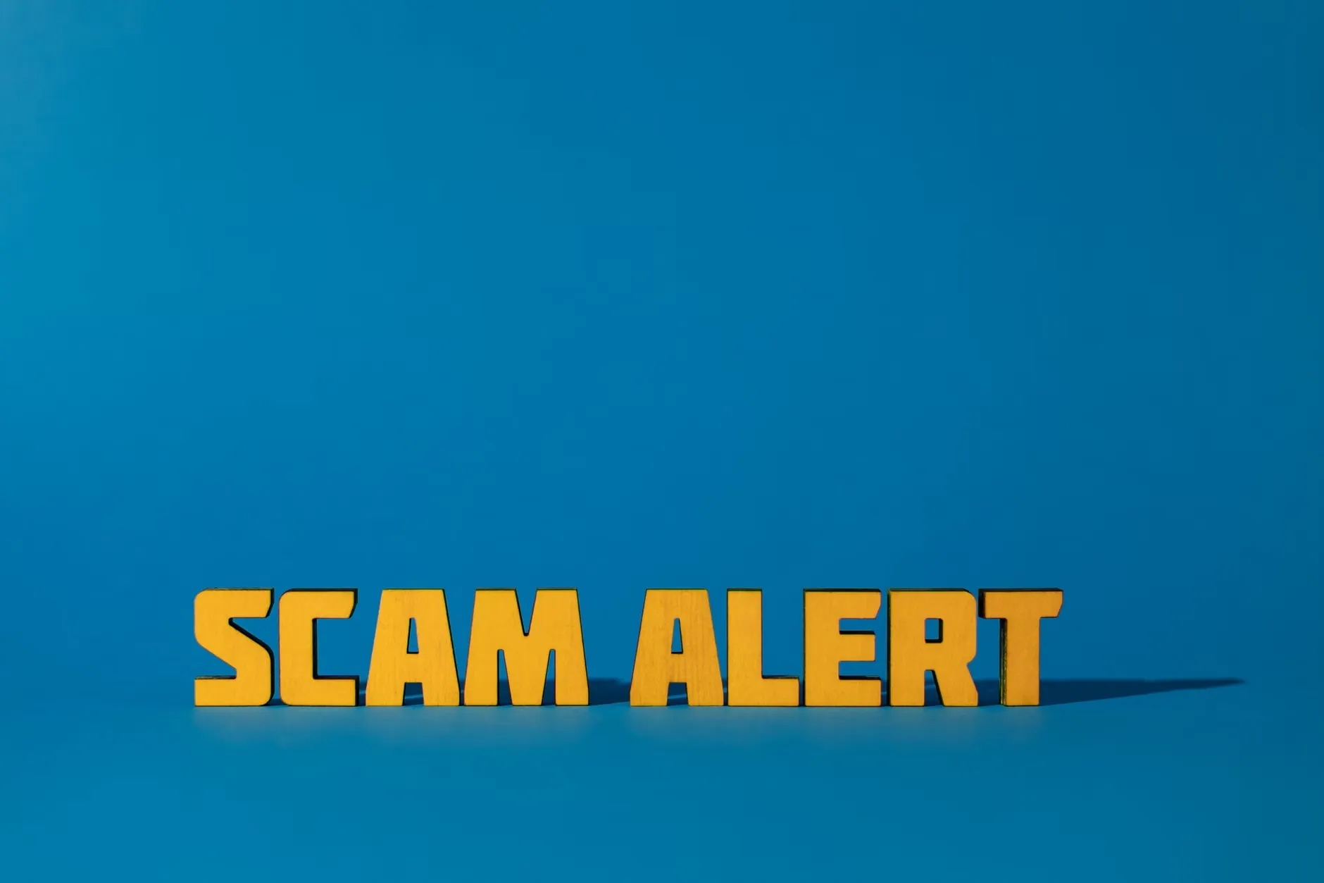 Et billede med gul tekst 'Scam Alert' på en blå baggrund, der advare mod svindel og bedrageri.