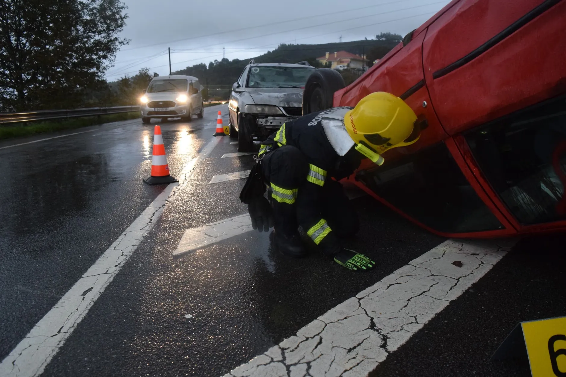 En brandmand er i færd med at hjælpe ved en bilulykke på en regnvej i Póvoa de Lanhoso, Braga, Portugal. Billedet viser den farlige situation og hjælpearbejdet.