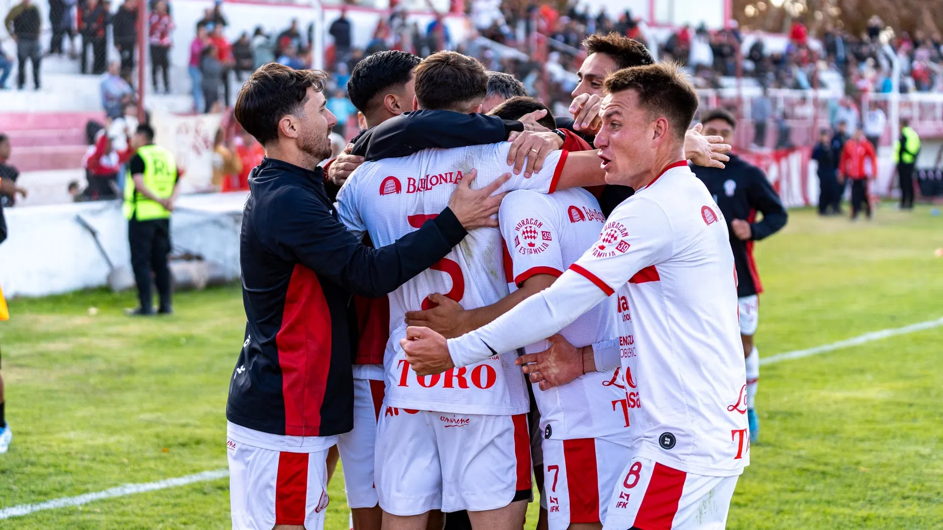 Et fodboldhold fejrer en scoring under en udendørs kamp. Billedet fanger energi, teamwork og glæden ved målet.