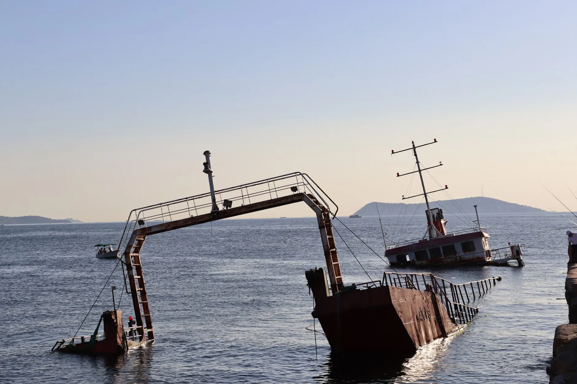 Et forladt skibsvrag delvist nedsænket i havet ved solnedgang, skabende en dramatisk havudsigt. Billedet viser en stille og øde scene.