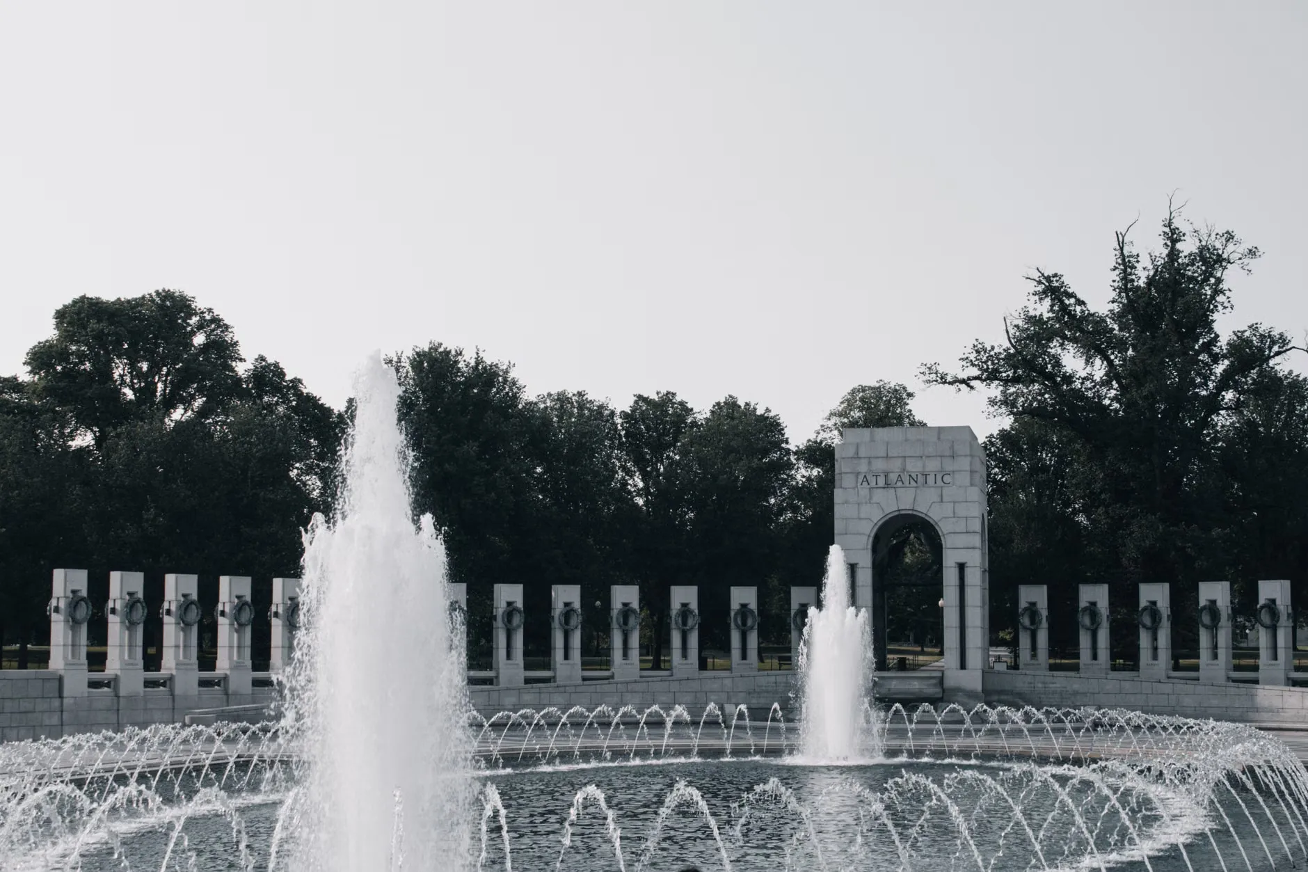 En fredfyldt scene fra National World War II Memorial i Washington D.C., hvor man ser Atlantic entrance og fountains. Billedet udstråler ro og kontemplation.