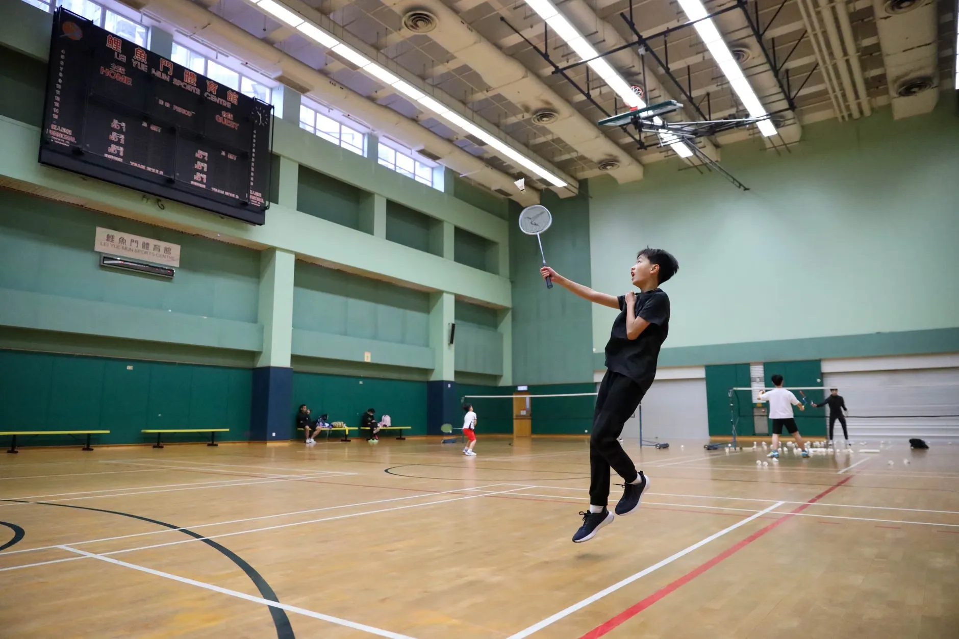 Sort-hvidt billede af en intens badmintonkamp indendørs med spillere og tilskuere. Kampen foregår i en stor hal med mange tilskuere.