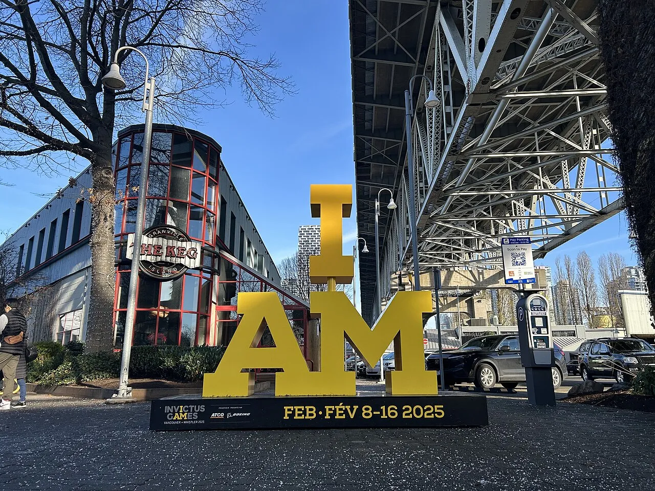 Et skilt med Invictus Games logoen under Granville Bridge på Granville Island, Vancouver. Skiltet symboliserer stædighed og mod.